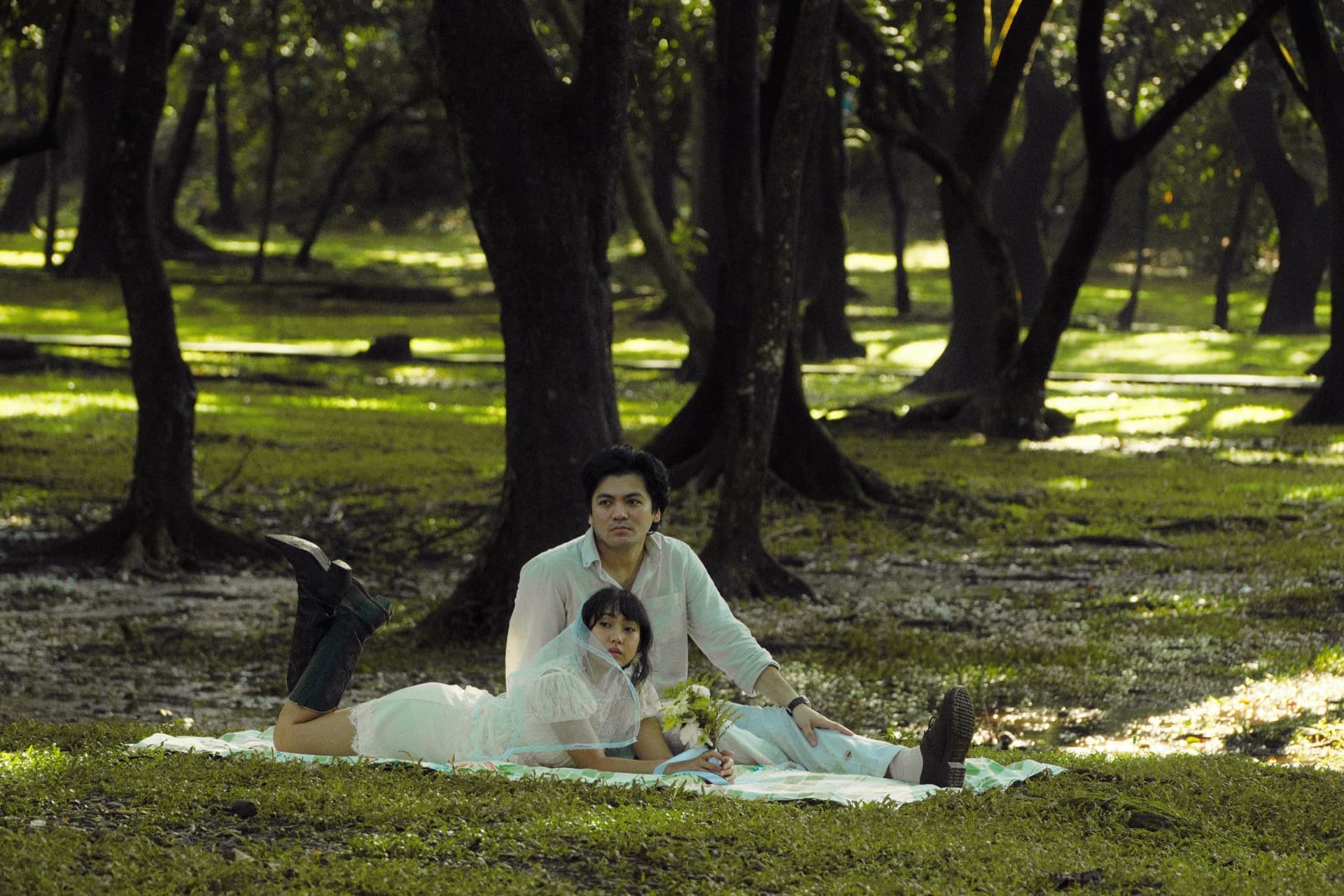 The couple resting on a picnic blanket beneath the trees